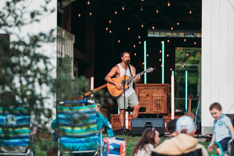 man playing guitar in front of a barn